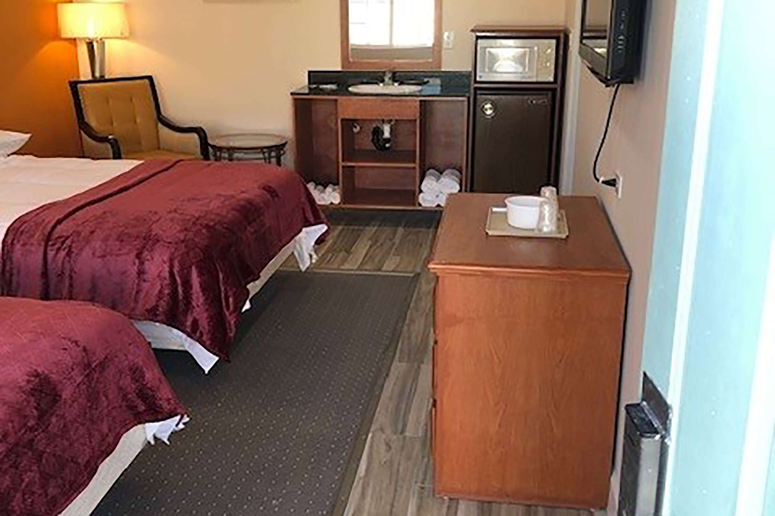 A hotel room with two beds, a desk, a chair, a microwave, and a television.