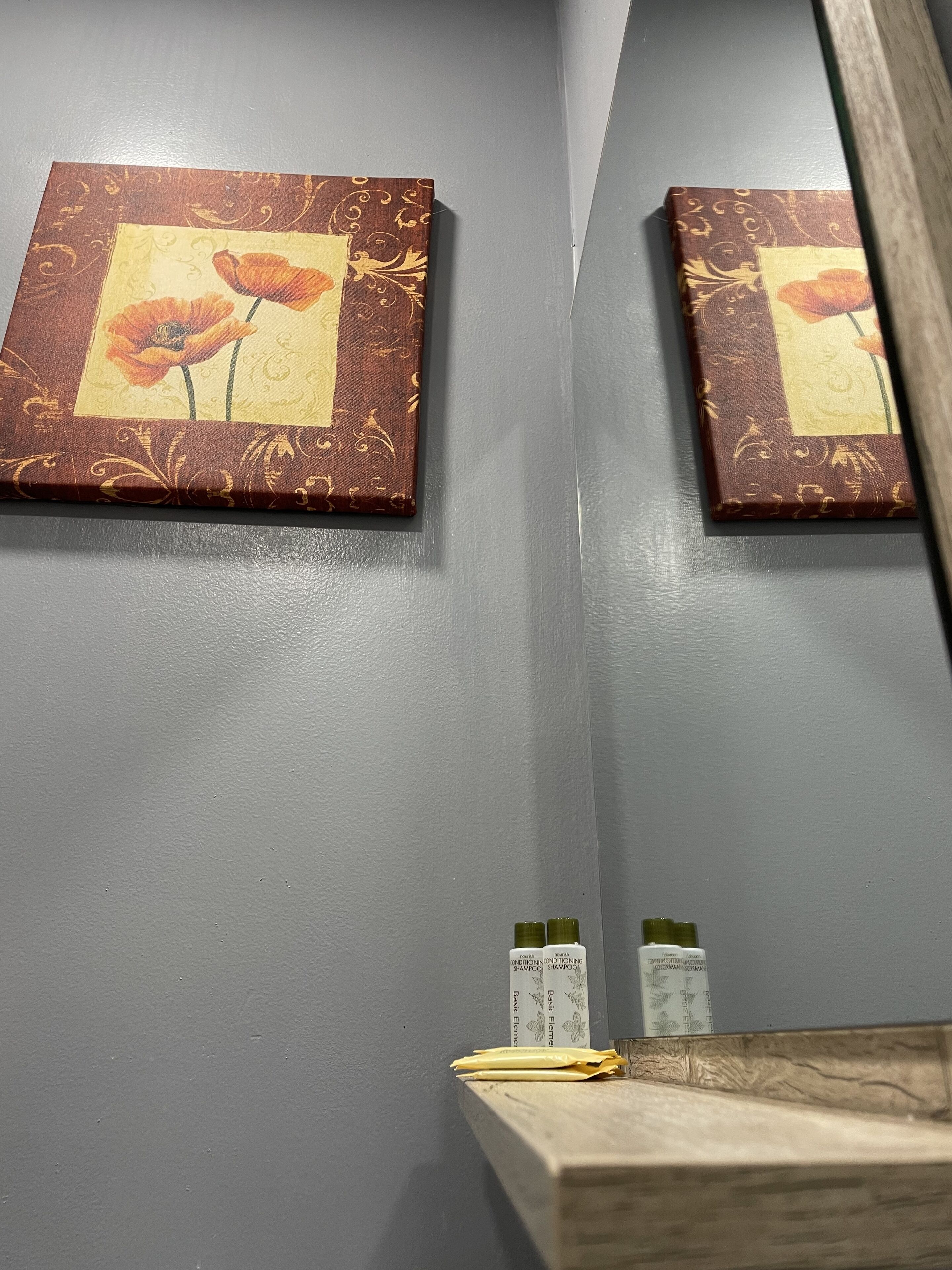 Un baño con un espejo, dos cuadros enmarcados de flores y un estante con artículos de tocador.