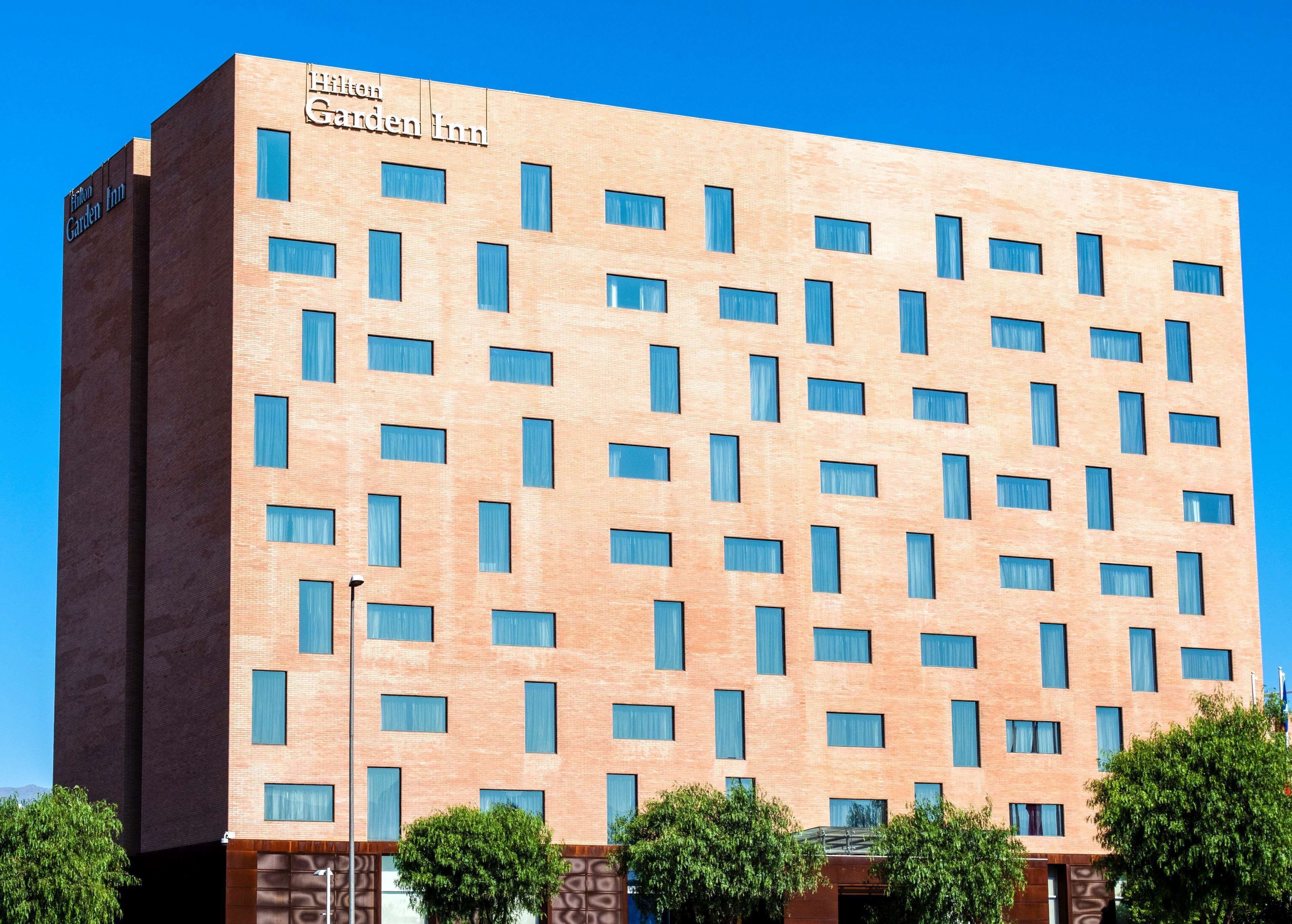 A Hilton Garden Inn hotel with a modern brick facade, numerous windows, and a clear blue sky in the background.
