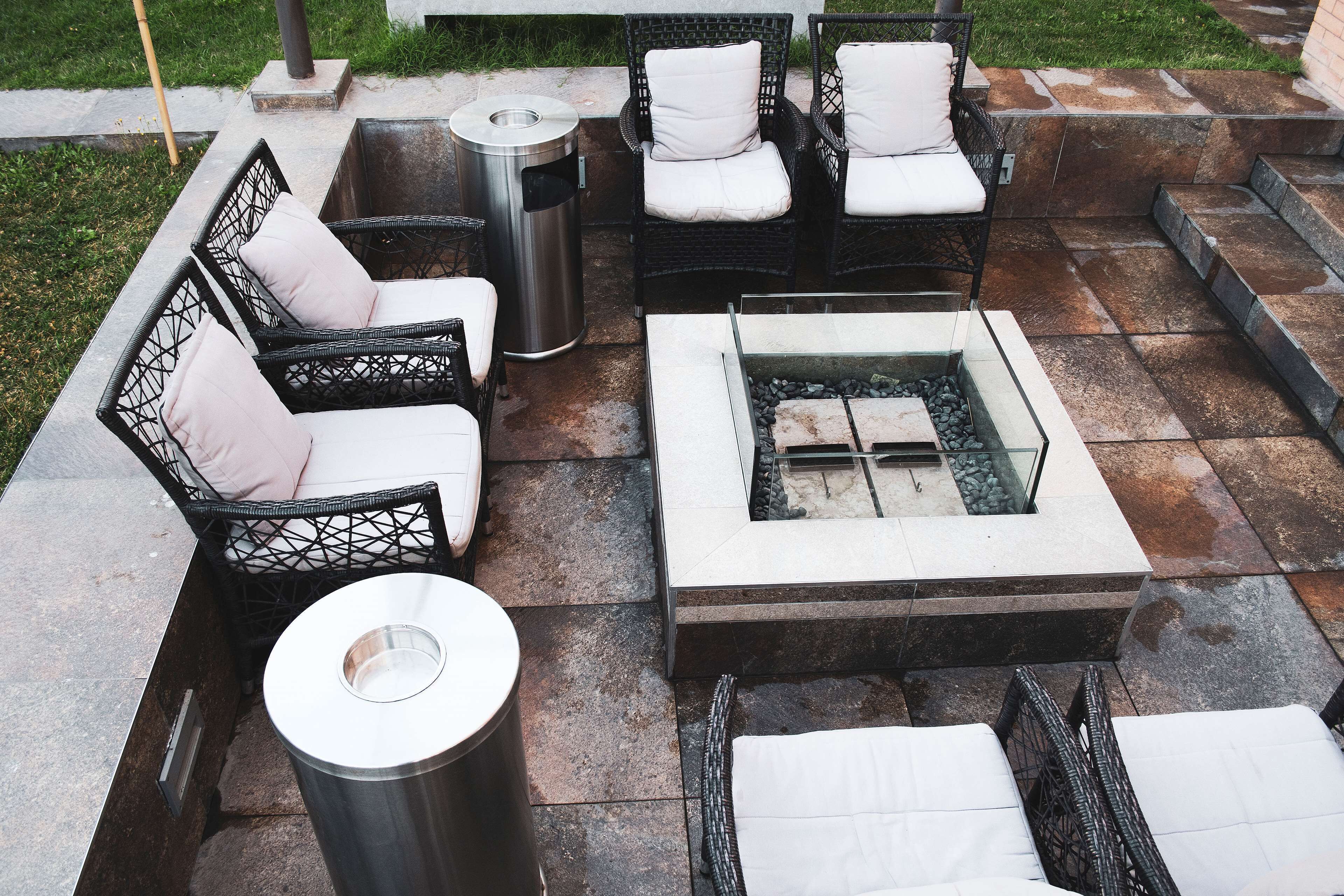Een terras buiten met rieten meubilair, een vuurkorf en een afvalbak.