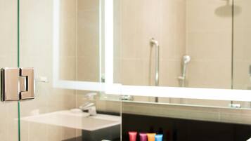 A modern bathroom with a glass shower enclosure, a large mirror, and a black countertop with toiletries.