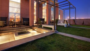 Ein moderner Außenbereich mit Terrasse, Glasveranda, Sitzgelegenheiten und einem Feuerstellelement.
