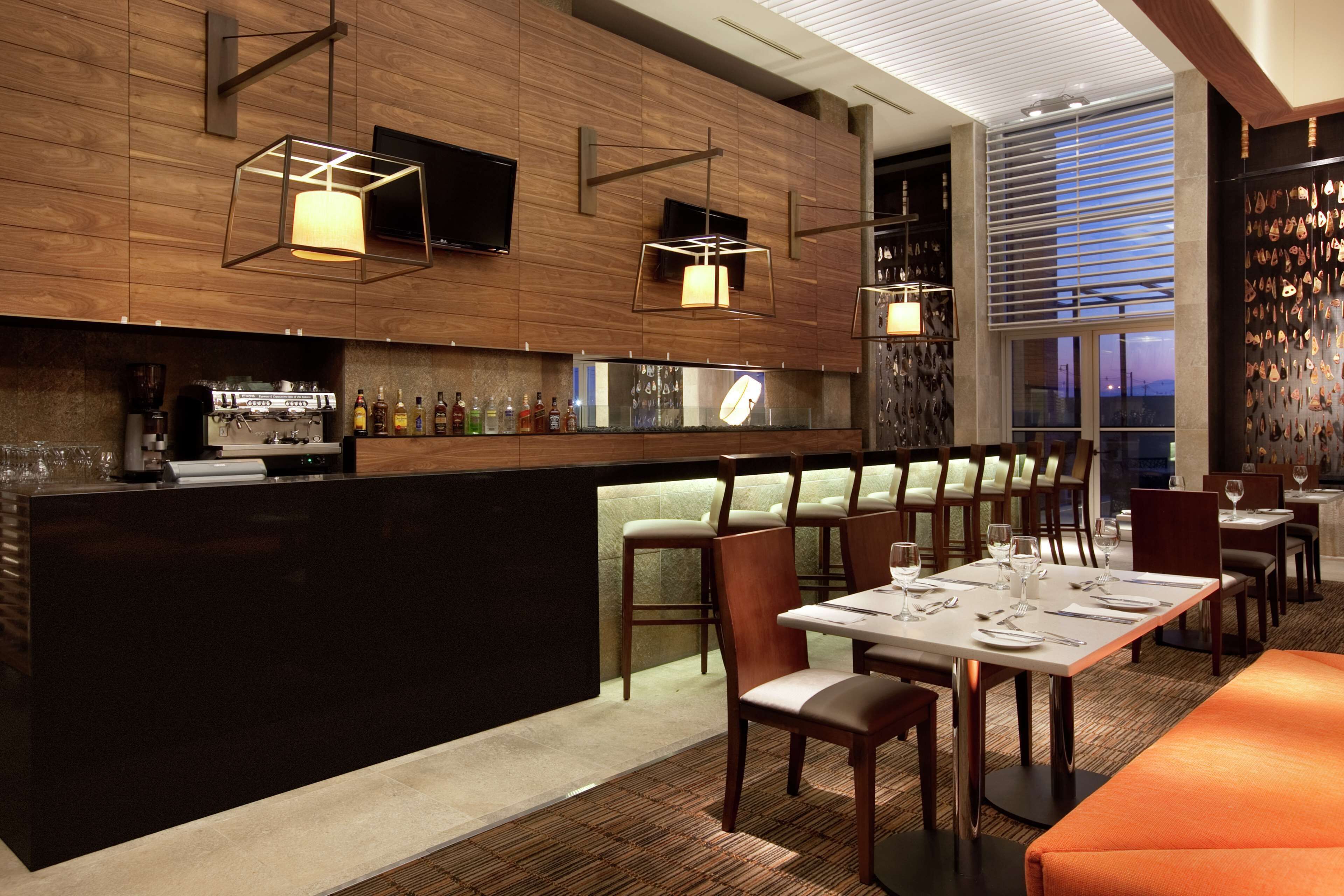 Zona de bar moderna amb panells de fusta, una barra amb eines de barman i seients per a clients.