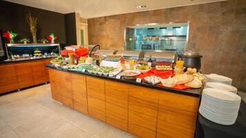 A buffet setup with various food items and a kitchen in the background.