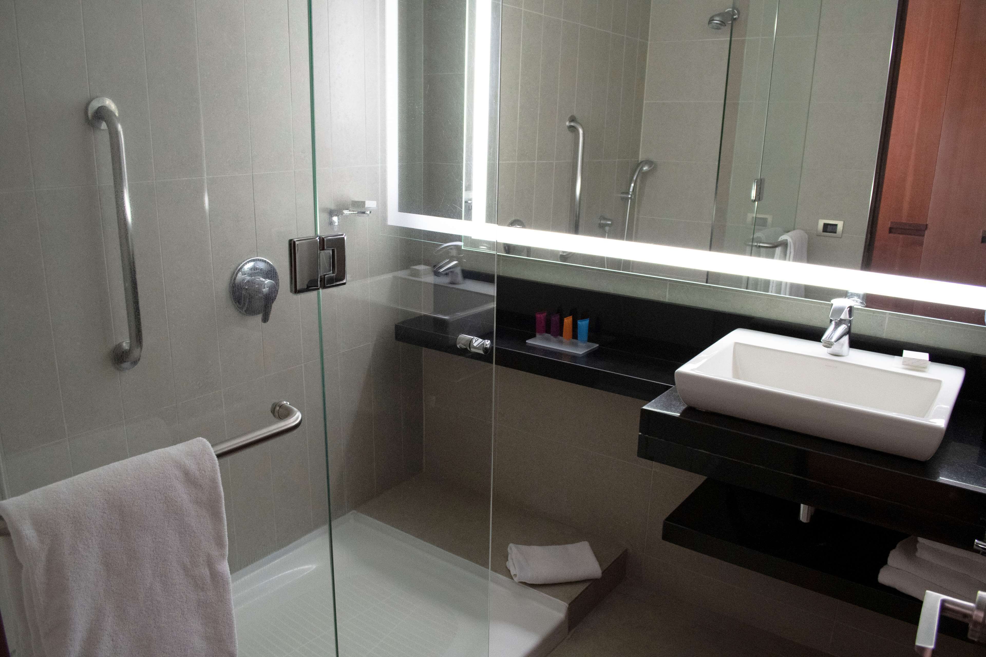 Ein modernes Badezimmer mit einer Duschkabine aus Glas, einem weißen Waschbecken und einem großen Spiegel.