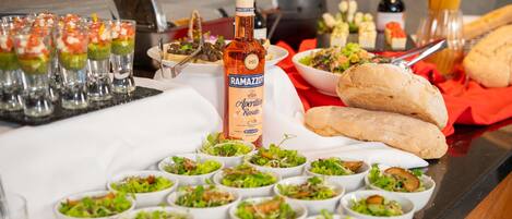 Una mesa de buffet con diversos platos, incluyendo ensaladas y pan, y una botella de Ramazzotti Aperitivo Rosato.