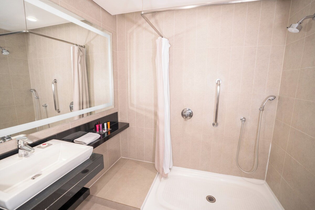 Un baño con ducha, lavabo, espejo y toallero.