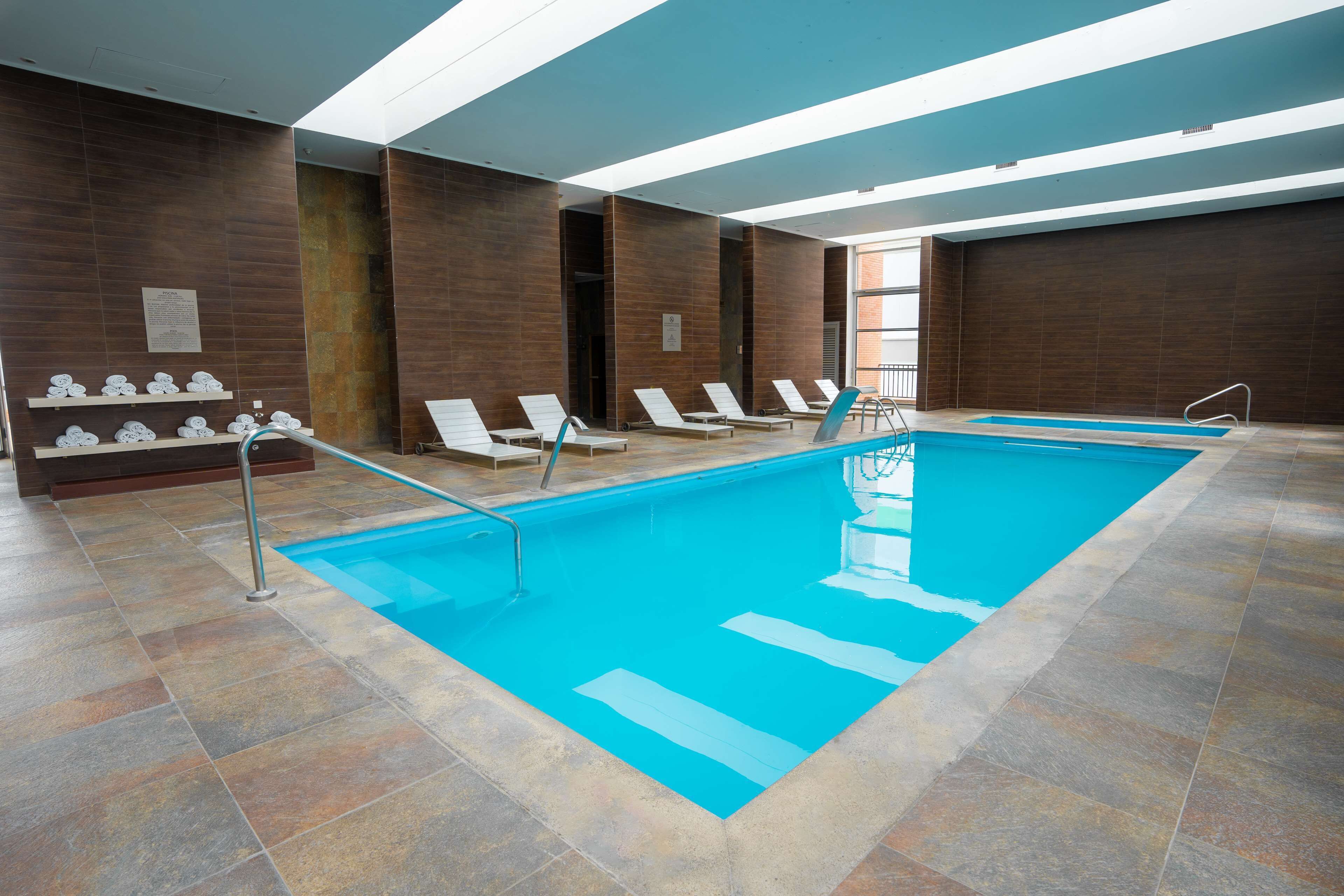 A swimming pool with lounge chairs, a tiled floor, and a wooden wall with a sign.
