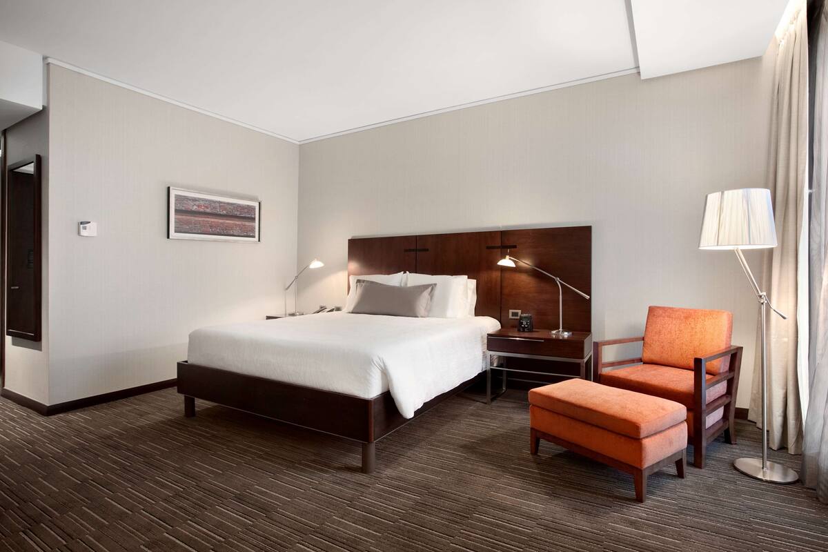 Una habitación de hotel con una cama grande, un escritorio, un sillón naranja y una lámpara.