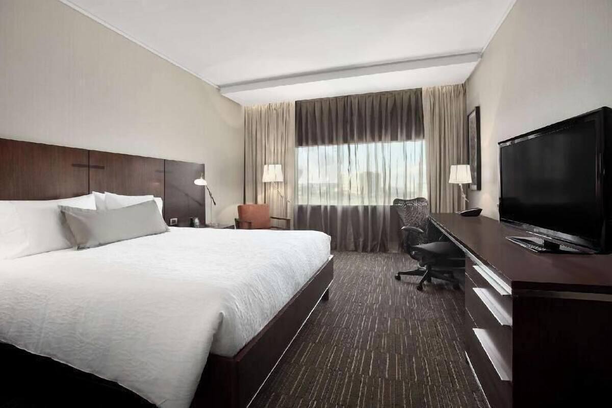 Una habitación de hotel con una cama grande, un escritorio con televisor y una ventana con cortinas.