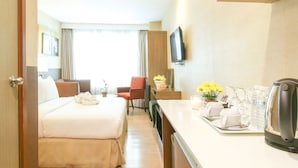 A hotel room with a bed, a desk, a chair, a television, and a tray with toiletries.
