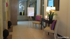 A hotel lobby with a reception desk, a whiteboard with information, a plant, and a mirror on the wall.