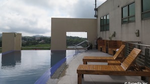 A rooftop pool area with wooden loungers, a view of the cityscape, and a satellite dish.