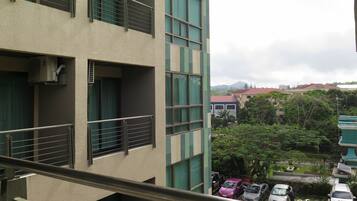 Un edificio de varios pisos con balcones, vista a vehículos estacionados y vegetación circundante.