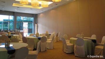 Un salón de banquetes con mesas redondas, sillas blancas y candelabros.
