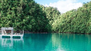 A deck with wicker chairs overlooking a turquoise lake, surrounded by lush greenery.