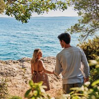 A couple standing on a rocky beach with the sea in the background.
