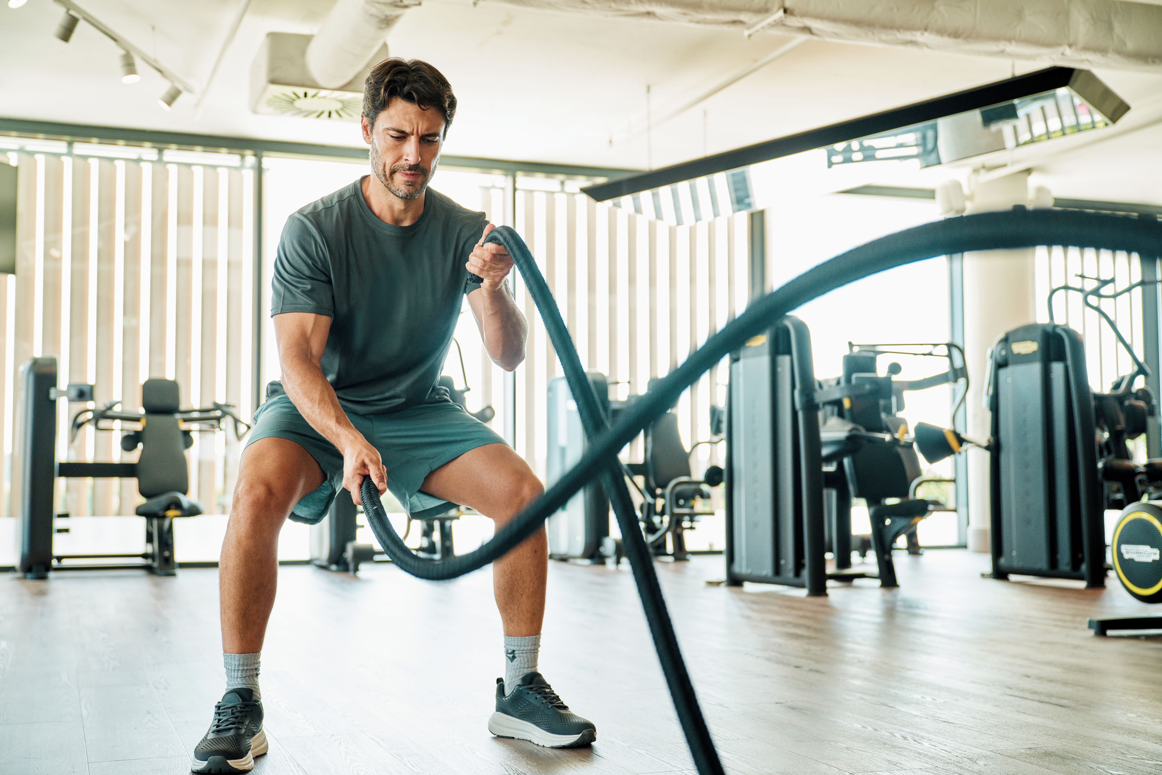 Eine Person fährt ein stationäres Fahrrad in einem Fitnessstudio, im Hintergrund sind Trainingsgeräte zu sehen.