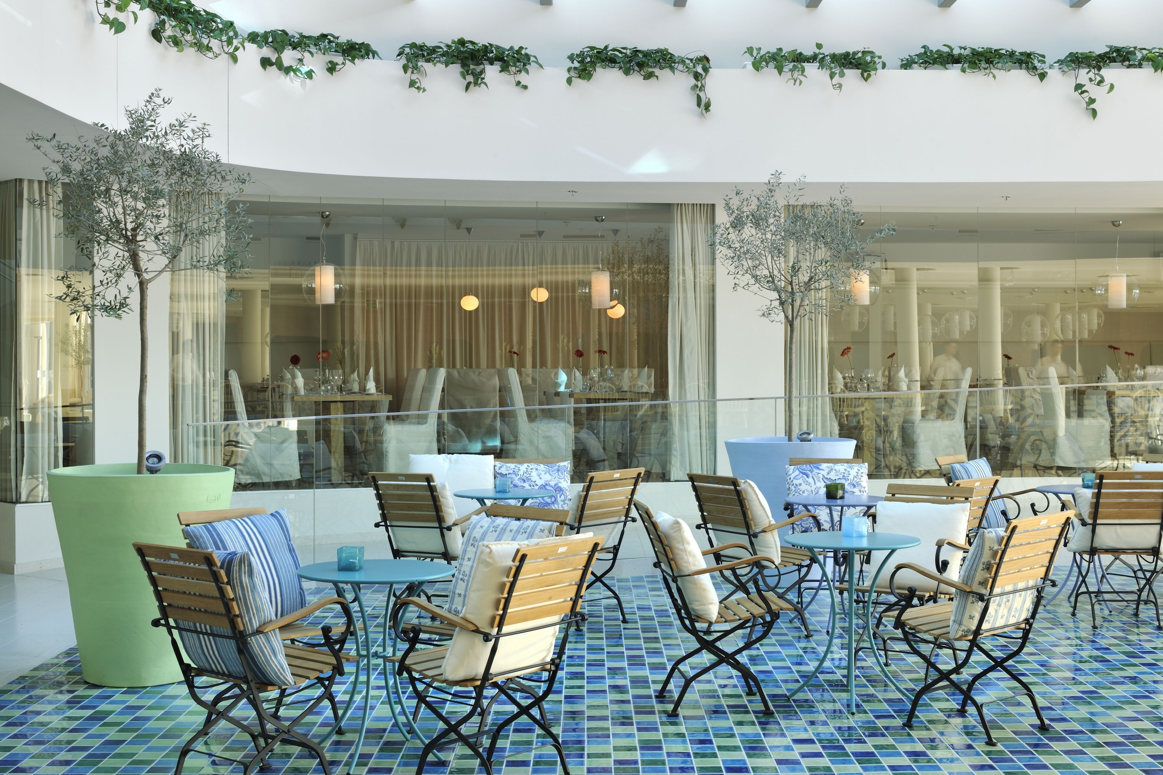 An indoor seating area with tables and chairs, large windows, and decorative plants.