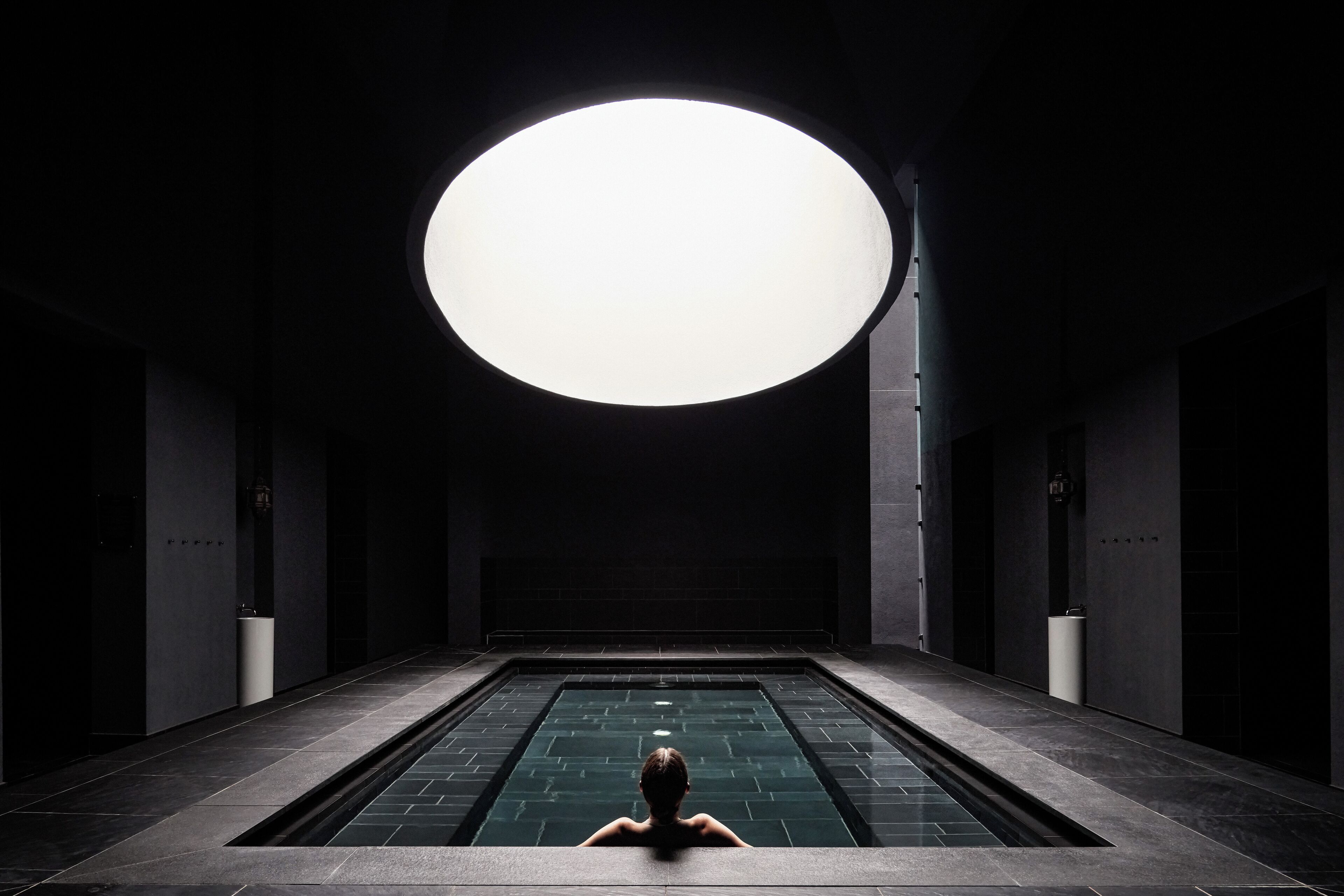 A person sitting in a dark room with a large circular light above them.