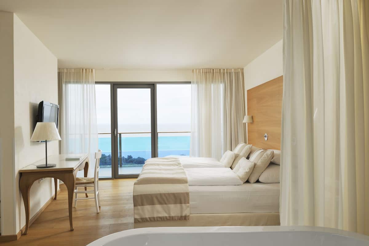 Een hotelkamer met een bed, een bureau, een stoel, een televisie en uitzicht op zee.