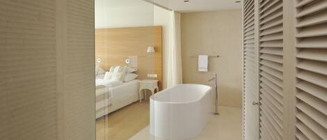 A modern bathroom with a freestanding bathtub, a wooden headboard, and a glass partition.