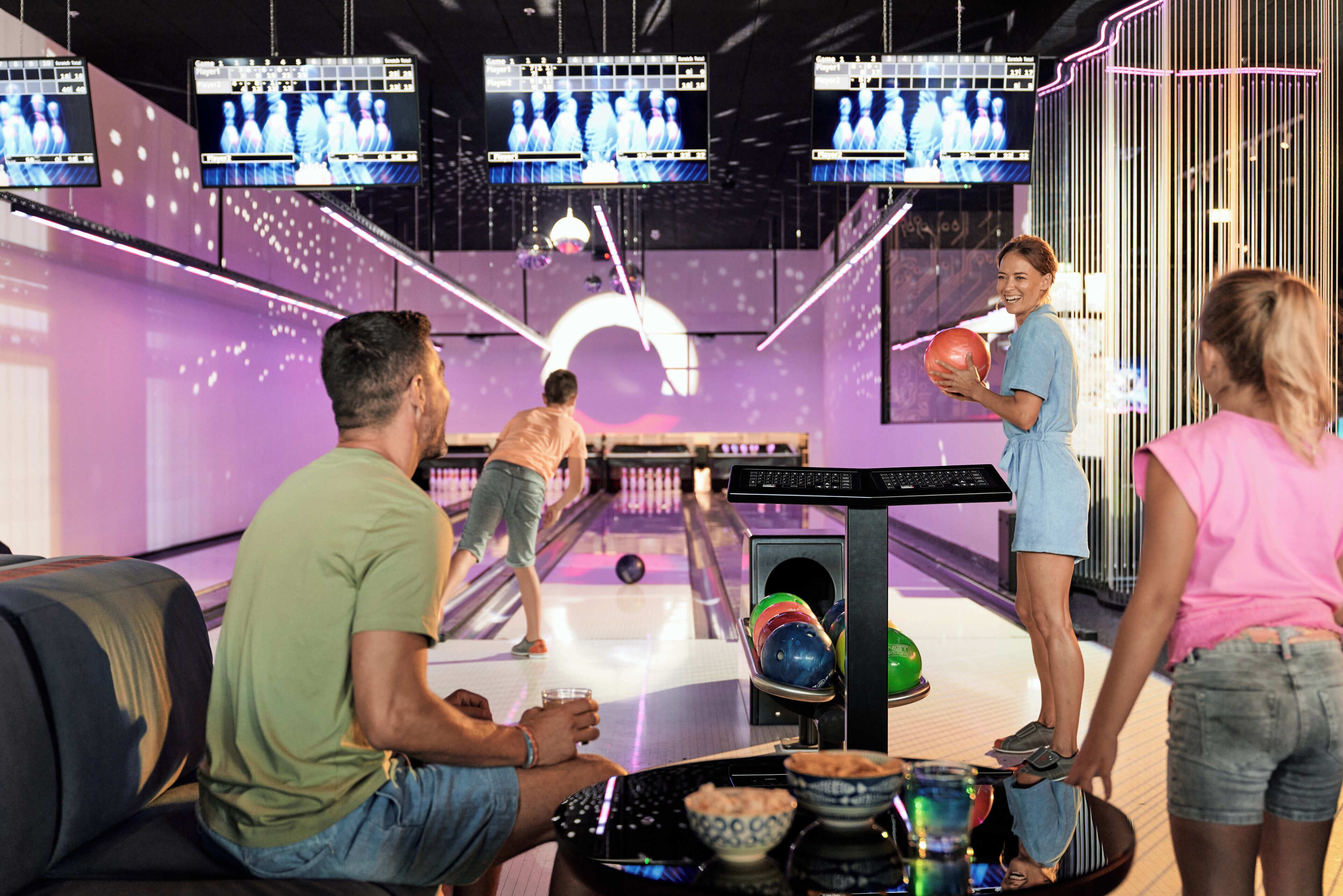 Een bowlinghal met meerdere banen, een bowlingbal en een persoon die aan het bowlen is.