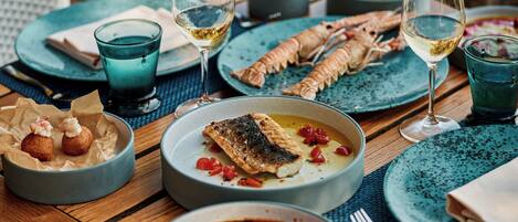 A dining table with various dishes, including seafood and a fish dish, accompanied by glasses of white wine.
