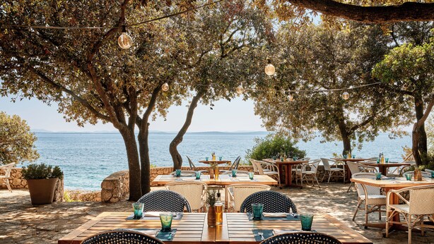An outdoor dining area with tables and chairs, overlooking a body of water. - Falkensteiner Hotel & Spa Iadera (Zadar)