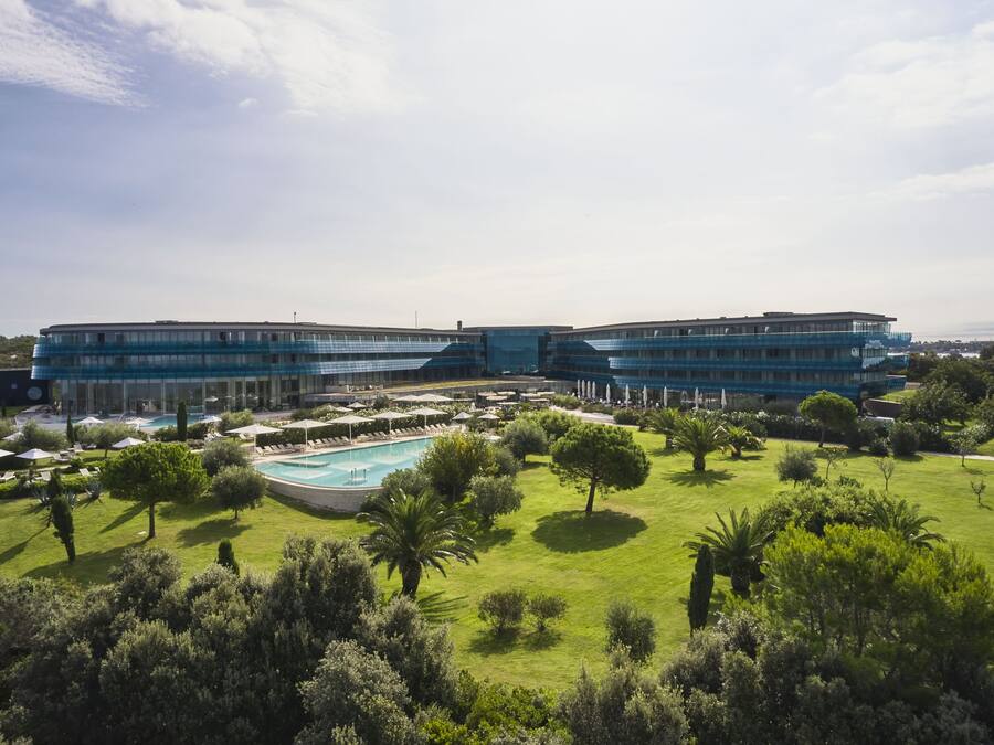 Un hotel moderno con una piscina amplia, césped verde exuberante y cielo despejado.