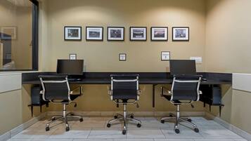 A conference room with three desks, each with a computer and a chair. There are four framed pictures on the wall, each labeled with a station number.