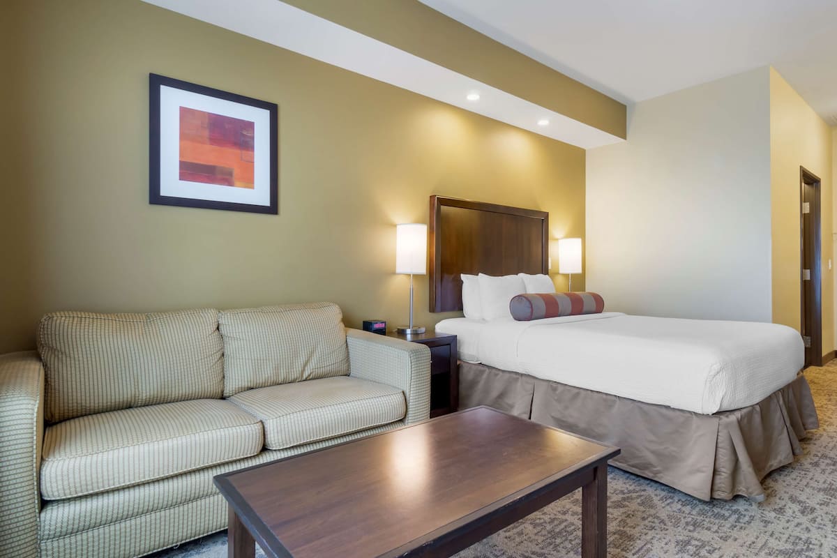 A hotel room with a bed, a sofa, a nightstand, and a lamp.