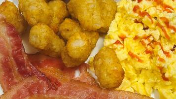 A plate with tater tots, scrambled eggs with ketchup, and bacon.
