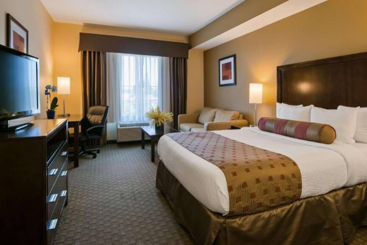 A hotel room with a large bed, a desk with a TV, a sofa, and a chair.