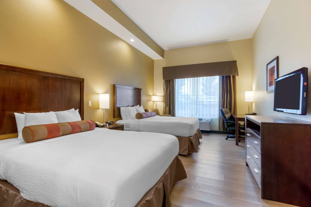 A hotel room with two beds, a desk, a television, and a chair.