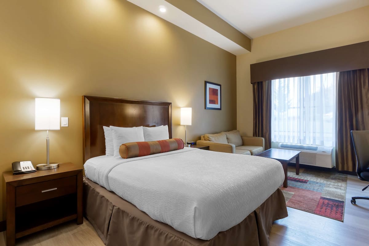 A hotel room with a large bed, bedside lamps, a desk, a chair, and a window with curtains.