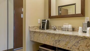 A bathroom with a marble countertop, a coffee maker, a sink, and a mirror.