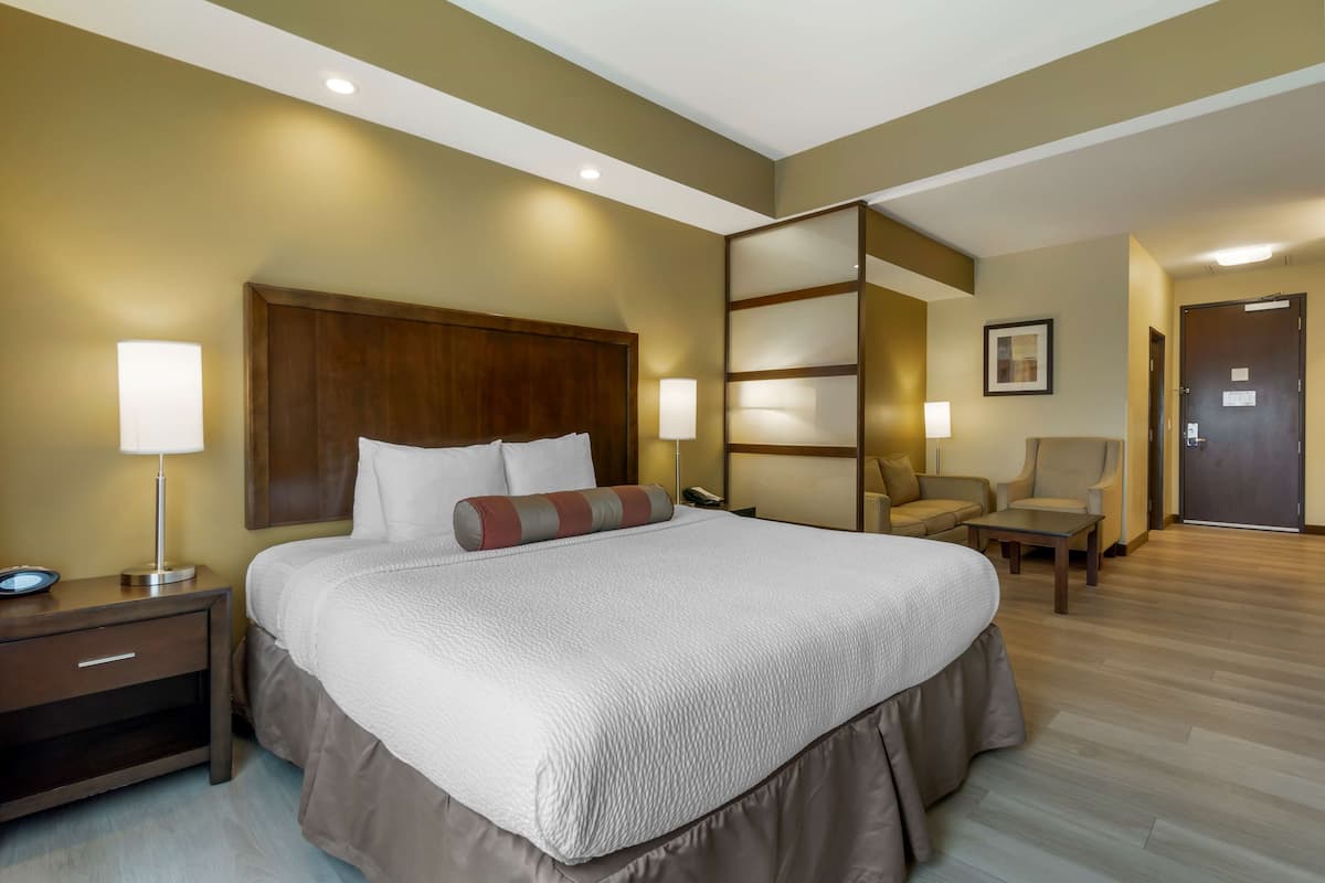 A hotel room with a large bed, bedside lamps, a chair, a desk, and a door.
