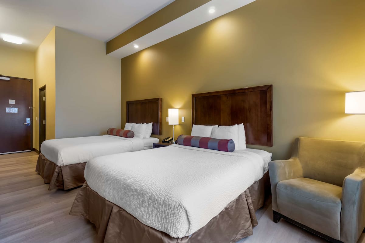 A hotel room with two beds, a chair, and a lamp.