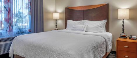 A hotel room with a large bed, two bedside lamps, a nightstand, and a window with curtains.