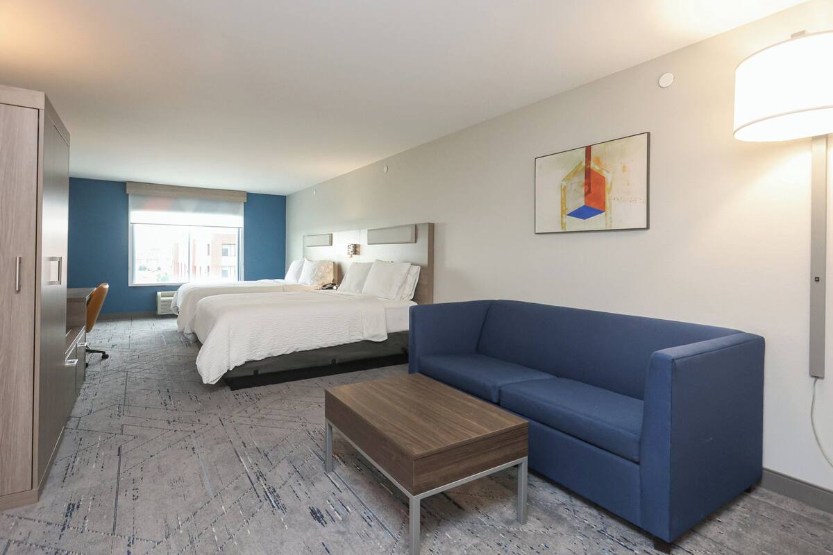 A hotel room with a bed, a blue sofa, a wooden coffee table, and a desk with a chair.