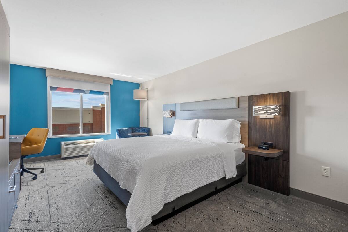 A modern hotel room with a large bed, a desk, a chair, and a view of the city.