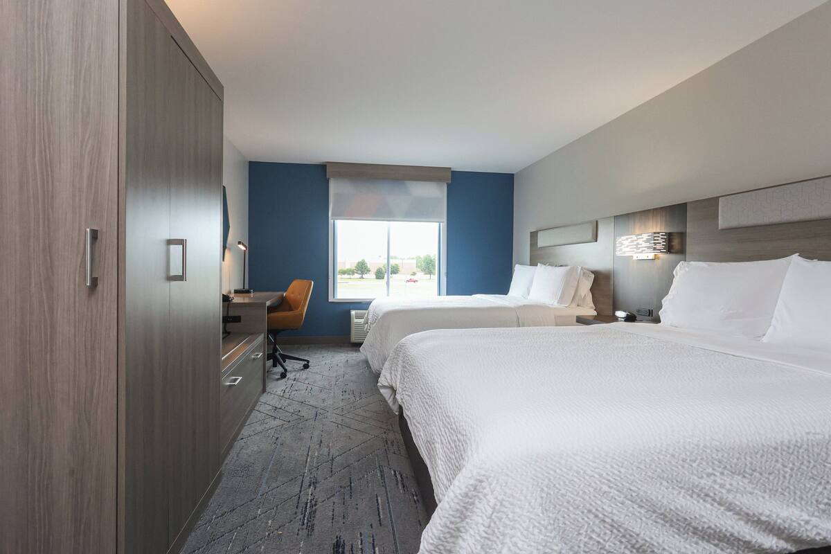 A hotel room with two beds, a desk, and a large window.