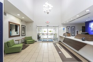 A reception area with a glass door entrance, green seating, a reception desk, and a chandelier. - Holiday Inn Express Tulsa South Bixby by IHG (Tulsa)