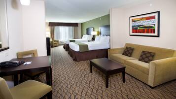 A hotel room with two beds, a sofa, a coffee table, and a desk with a telephone.
