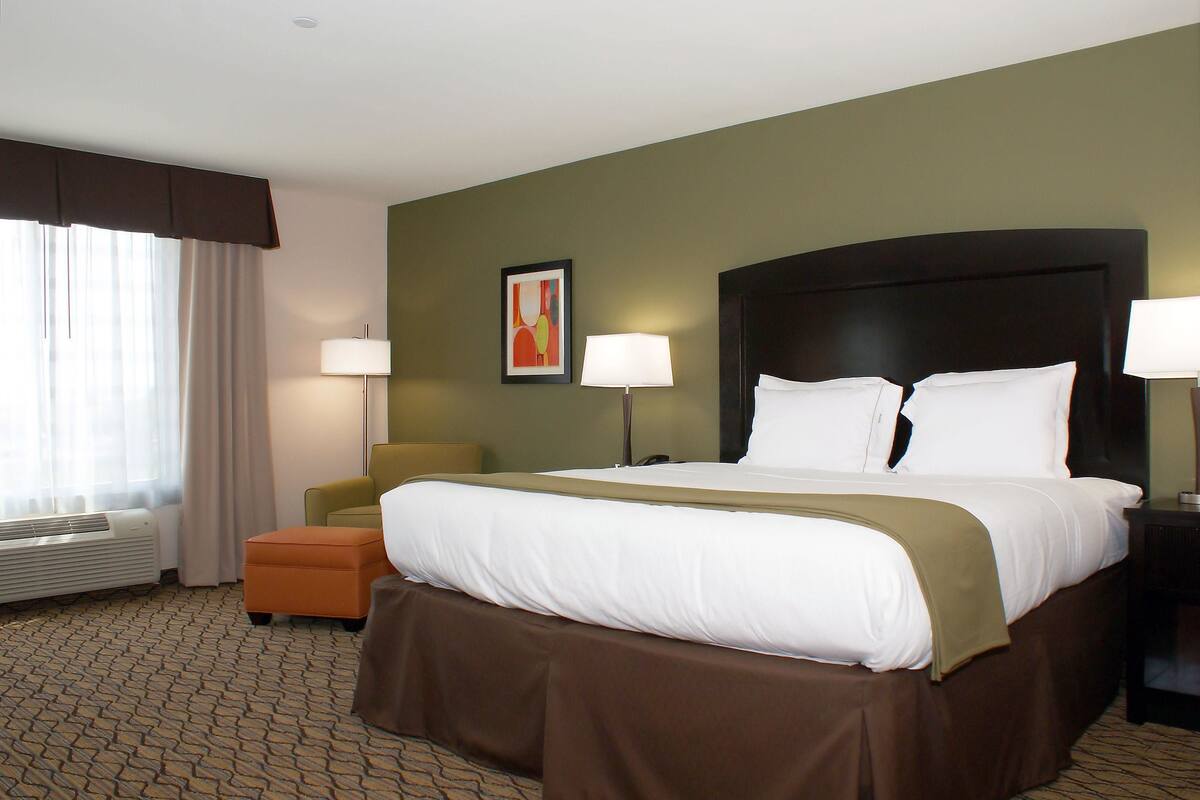 A hotel room with a large bed, a chair, a desk, and a window with curtains.