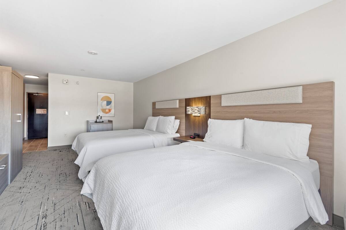 A hotel room with two beds, a nightstand, a wall-mounted light, and a door leading to another room.