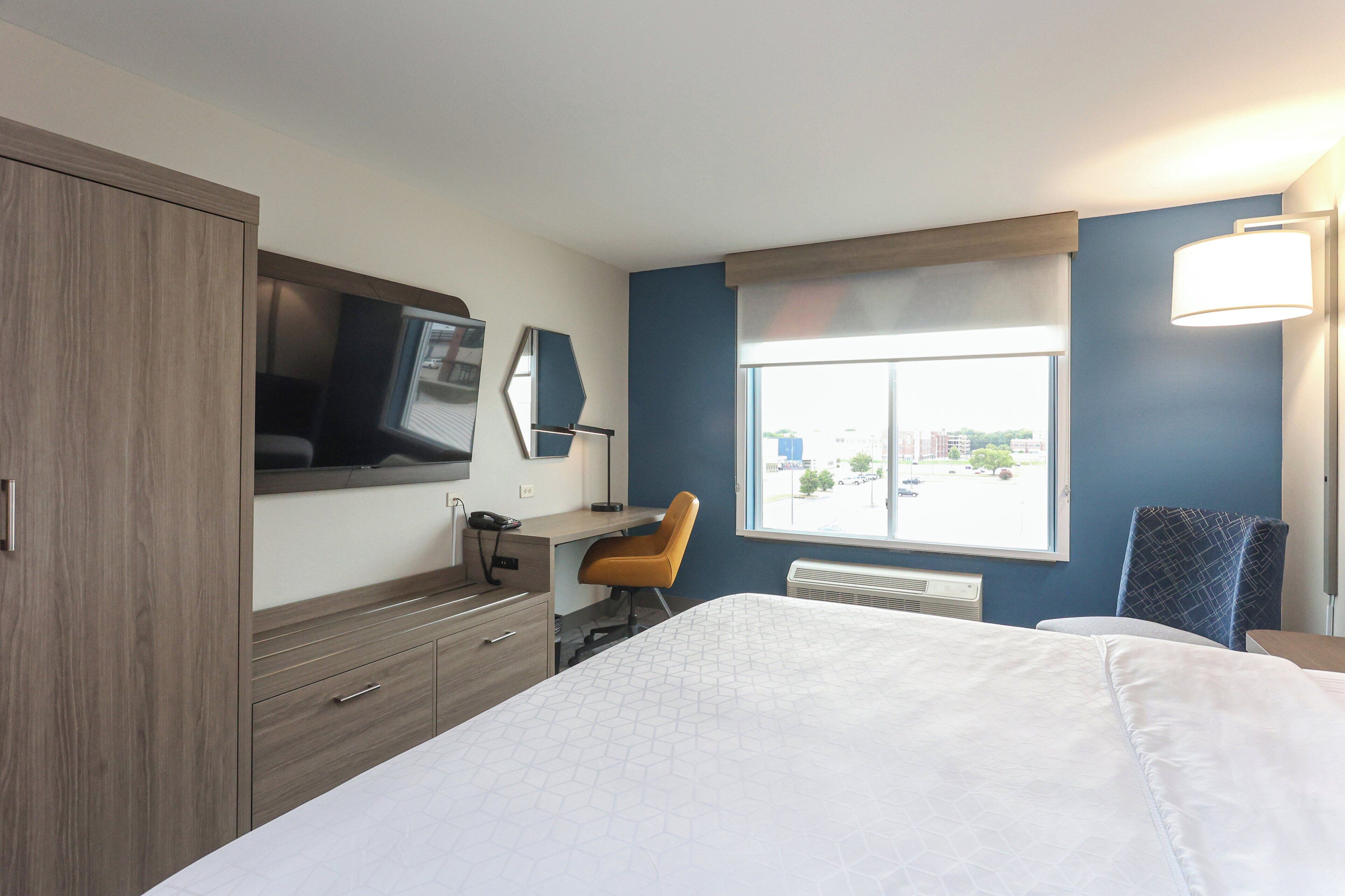 A hotel room with a bed, a desk, a chair, a TV, and a window with a city view.
