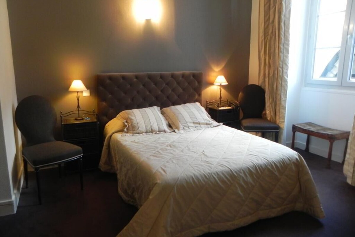A bedroom with a large bed, two bedside lamps, a chair, and a small table.