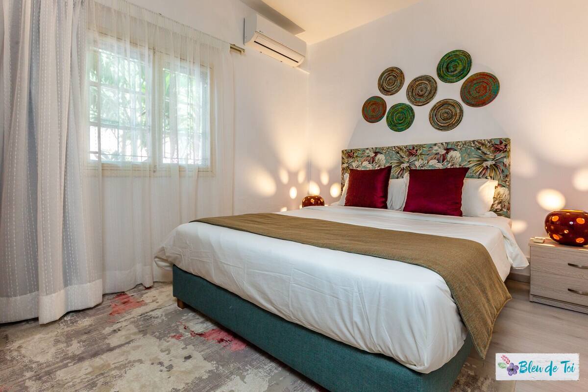 A bedroom with a bed, curtains, a headboard with a floral pattern, and wall decor.